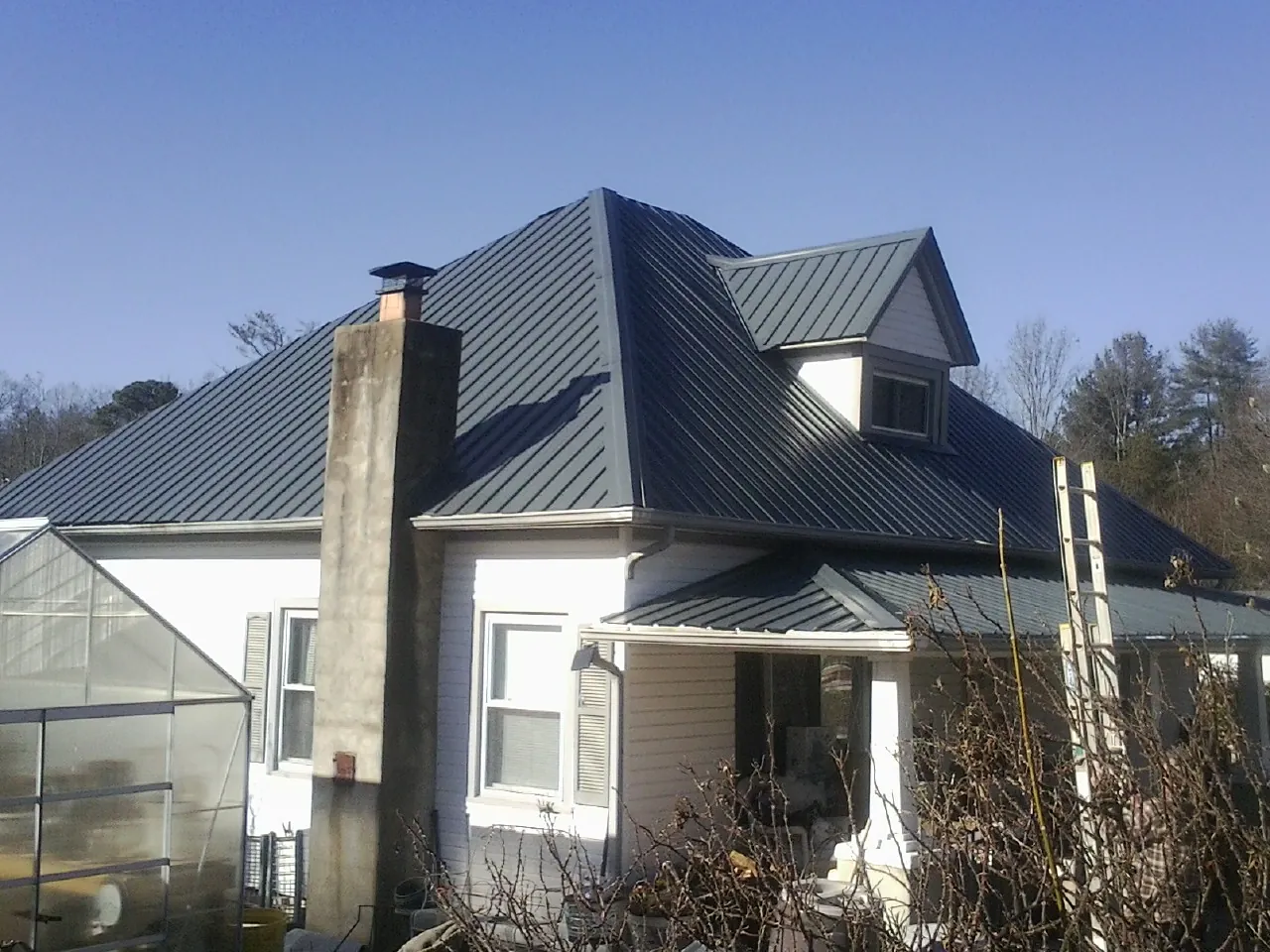 Dark blue standing seam metal roof on a white farmhouse with dormer — Slate & Tile Roof Repair by Roofing Brothers in Huxley
