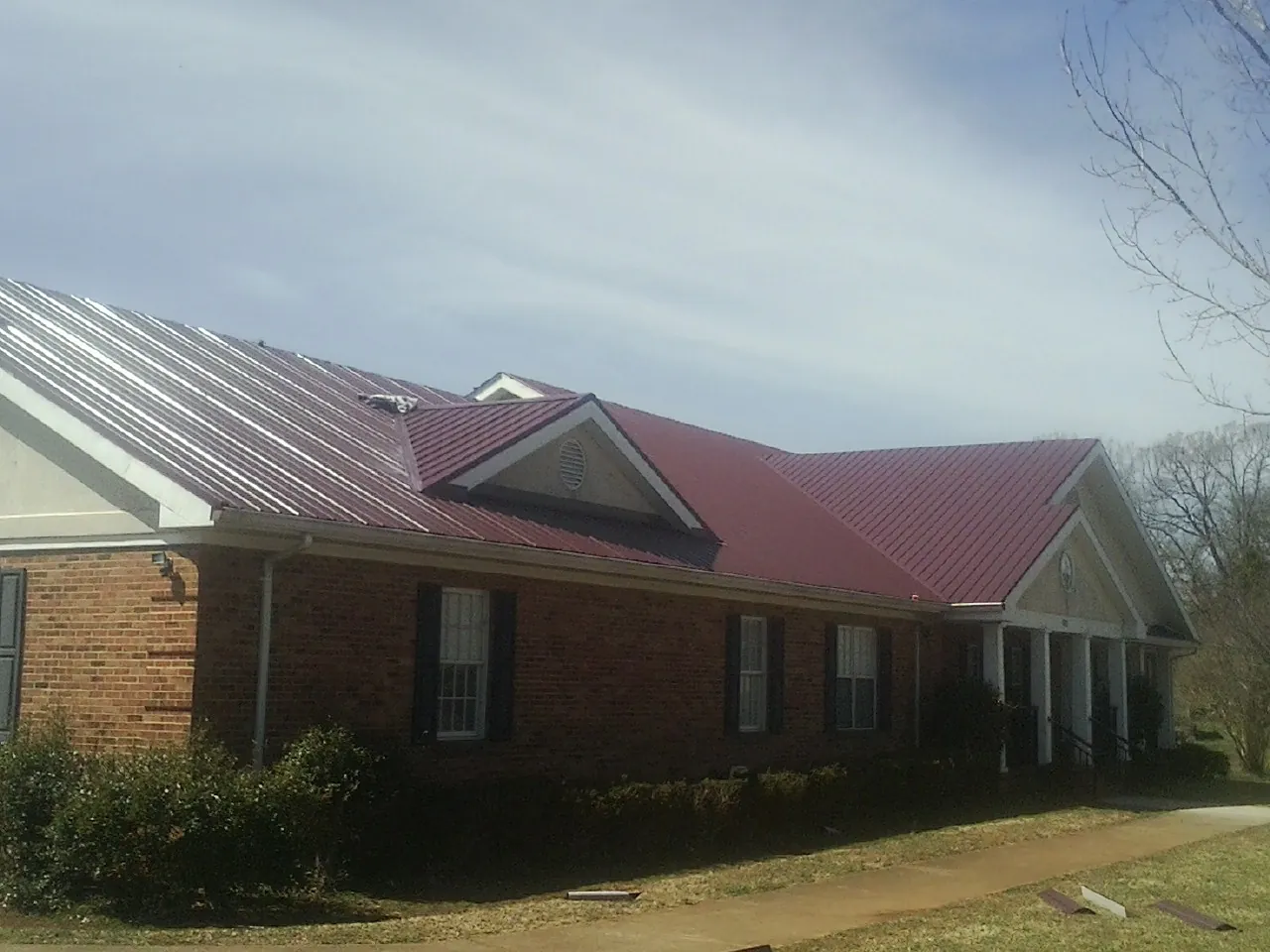 Red metal roof with gabled entries on a long brick building, from a Hail Damage Roof Repair job in Huxley