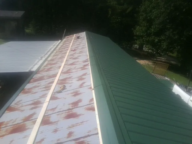 Old rusted panels beside newly installed green metal roofing — Wind Damage Roof Repair by Roofing Brothers in Huxley