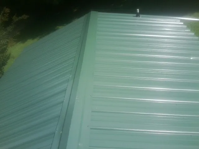 New green metal panels meeting at the ridge of a roof — Flat Roof Repair work by our crew in Huxley