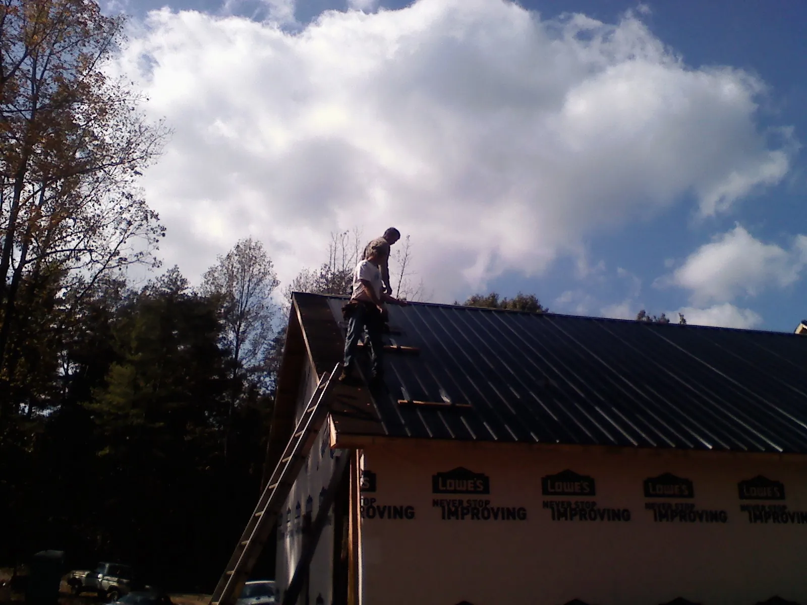 Roofer fastening dark metal panels high against a cloudy sky, from a Roof Inspection job in Huxley