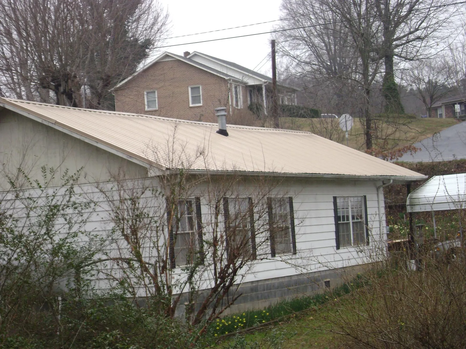 Tan metal roof on a white sided house set into a hillside — Commercial Roofing by Roofing Brothers in Huxley