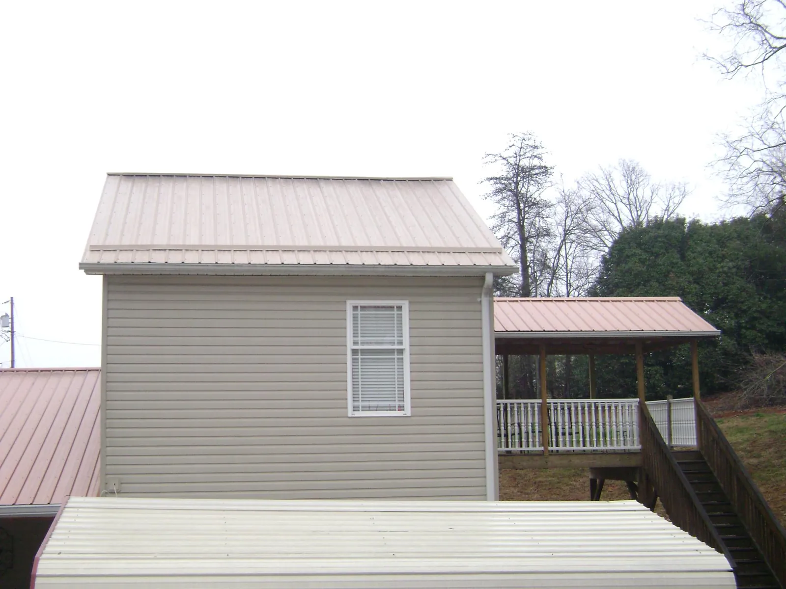 Tan metal roofs on a two story addition and attached porch, from a Roof Replacement job in Huxley