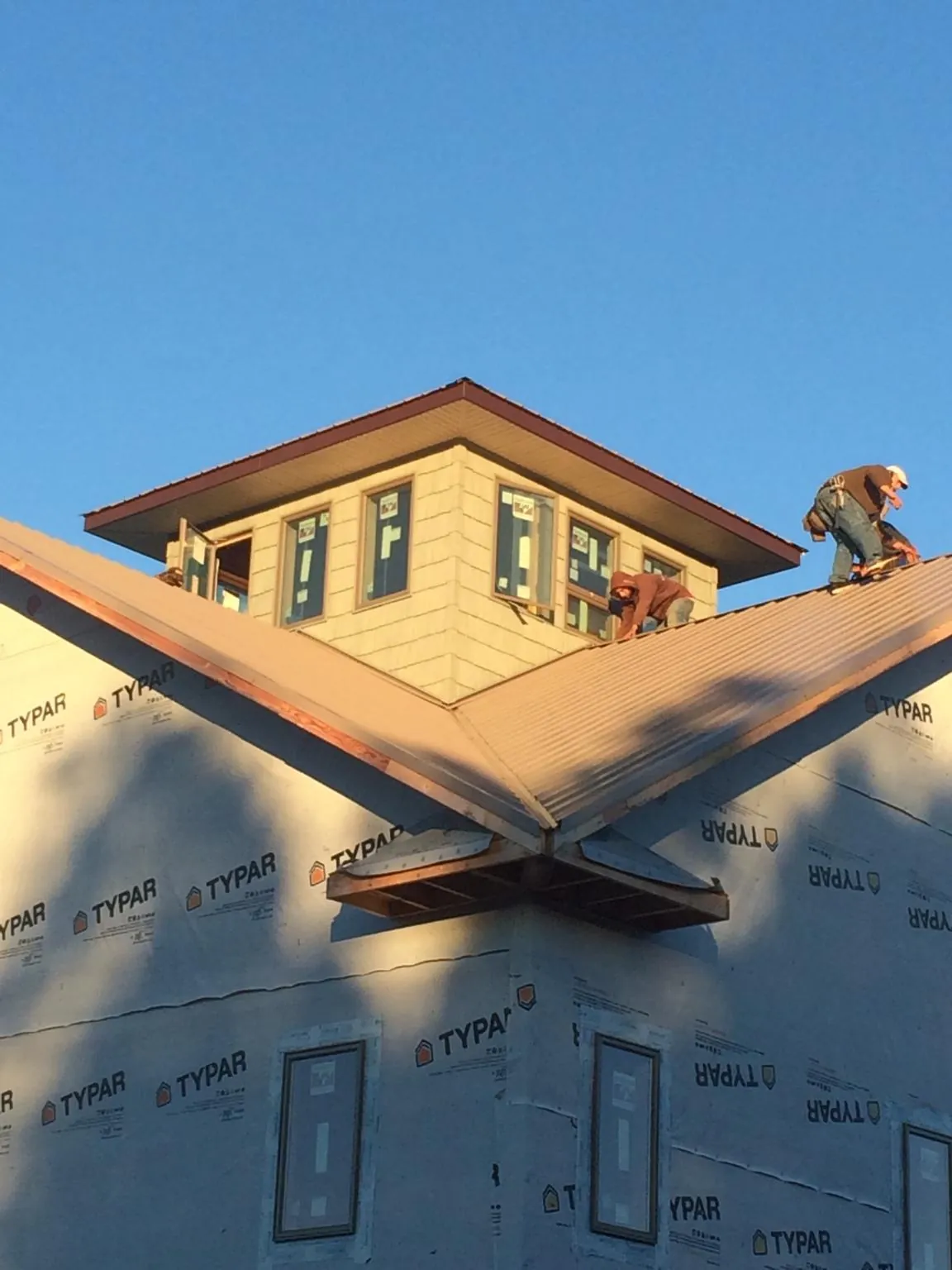 Roofers working around a rooftop cupola on a new metal roof at sunset — Roof Waterproofing in Huxley by Roofing Brothers
